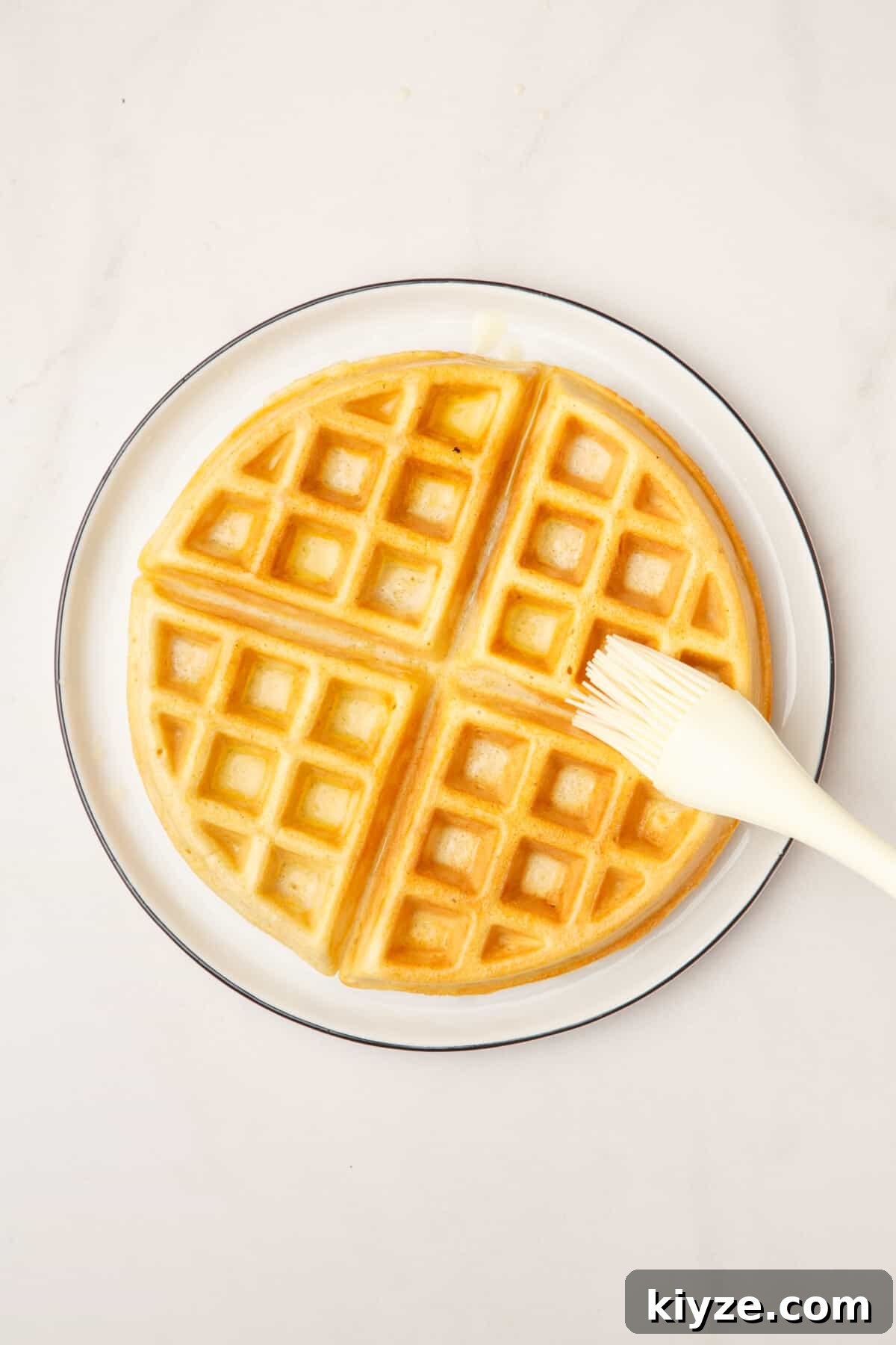 Crispy Cinnamon Churro Waffles Recipe 7 kitchen brush dousing a waffle with butter.