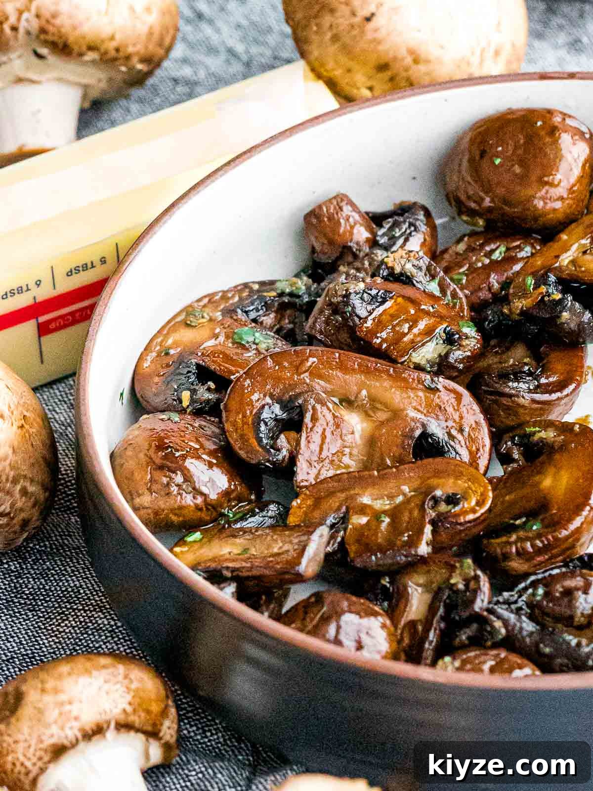 Garlic Butter Sautéed Mushrooms Recipe — Quick Flavorful Side 4 golden brown garlic butter mushrooms in a bowl next to a stick of butter