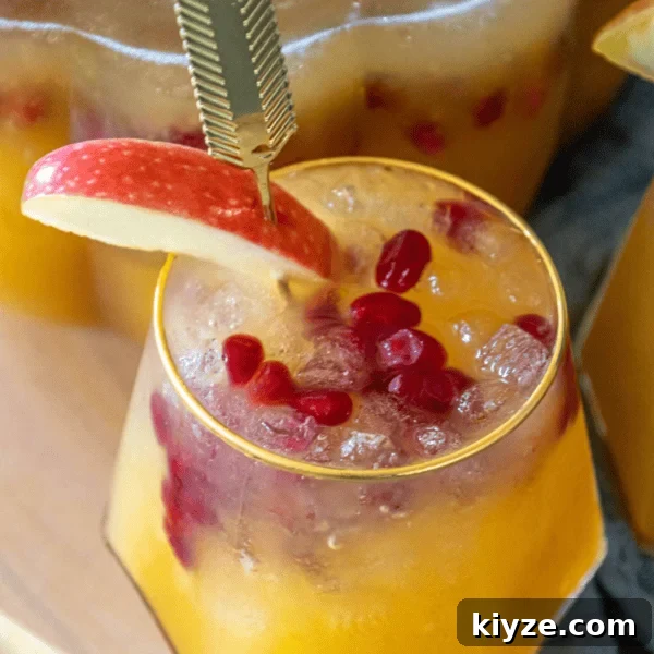 A yellow drink with pomegranate seeds and apple slice