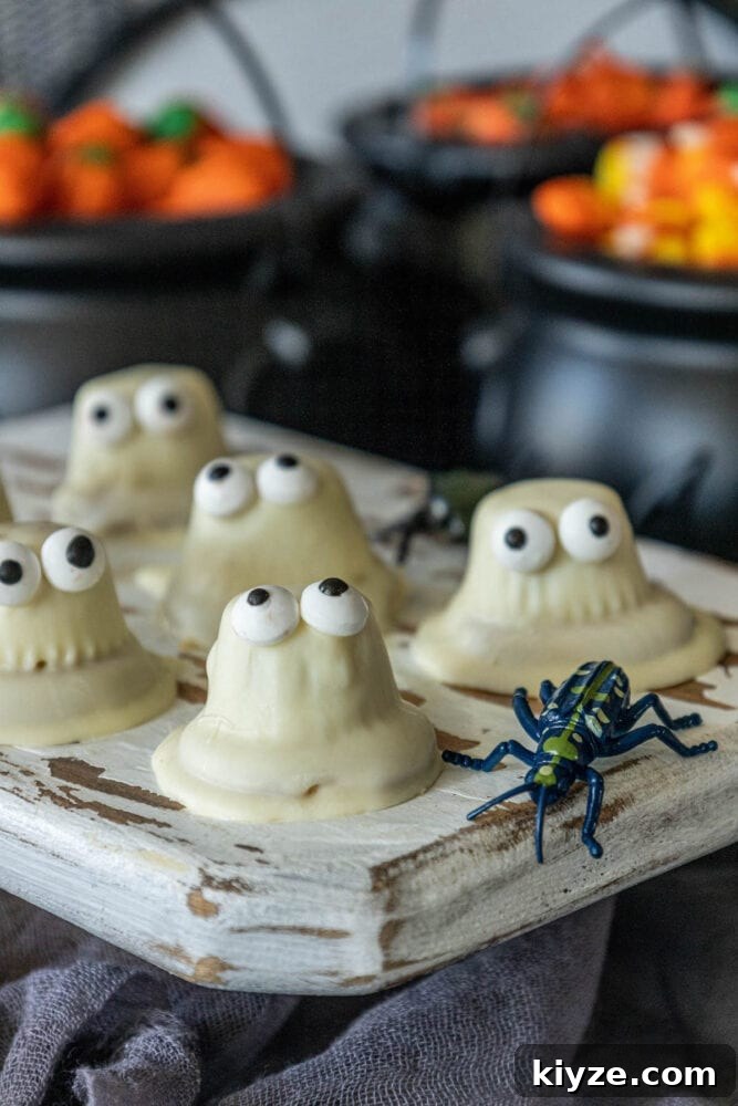 White Chocolate-Dipped Ghost Cookies: Spooky Halloween Treats 4 Halloween cupcakes with eyes and white chocolate dipped ghost cookies on a tray.