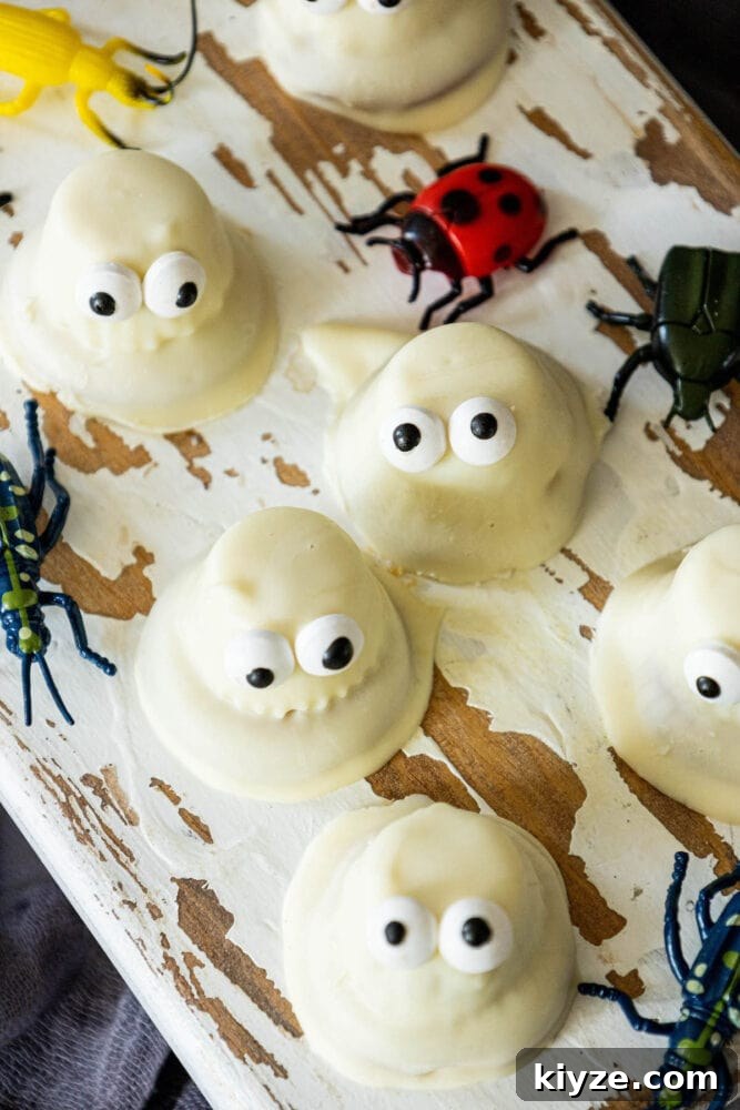 White Chocolate-Dipped Ghost Cookies: Spooky Halloween Treats 5 White chocolate dipped ghost cookies with eyes and insects on a wooden board.