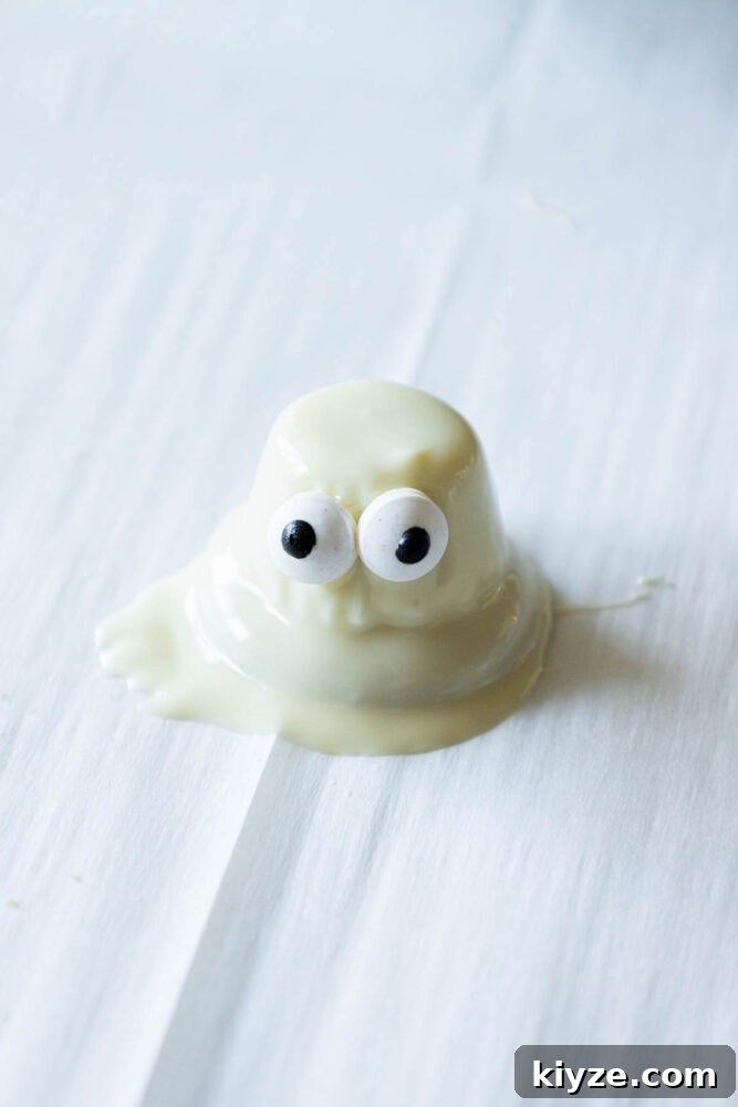 White Chocolate-Dipped Ghost Cookies: Spooky Halloween Treats 7 dipped cookie with candy eyes on parchment paper