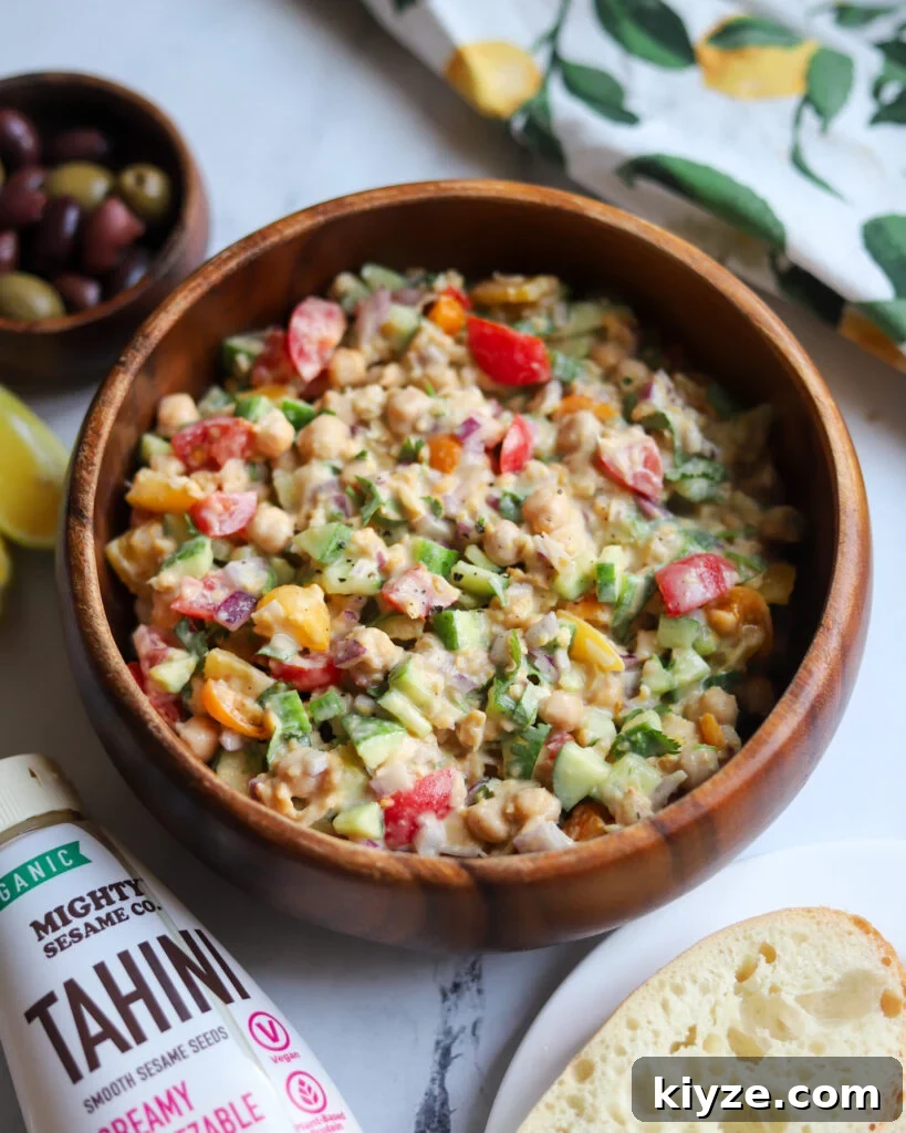 18 Flavorful Vegan Bean Salad Recipes for Every Occasion 12 wooden serving bowl with chickpea tahini salad next to pita bread, a bottle of tahini, and olives.