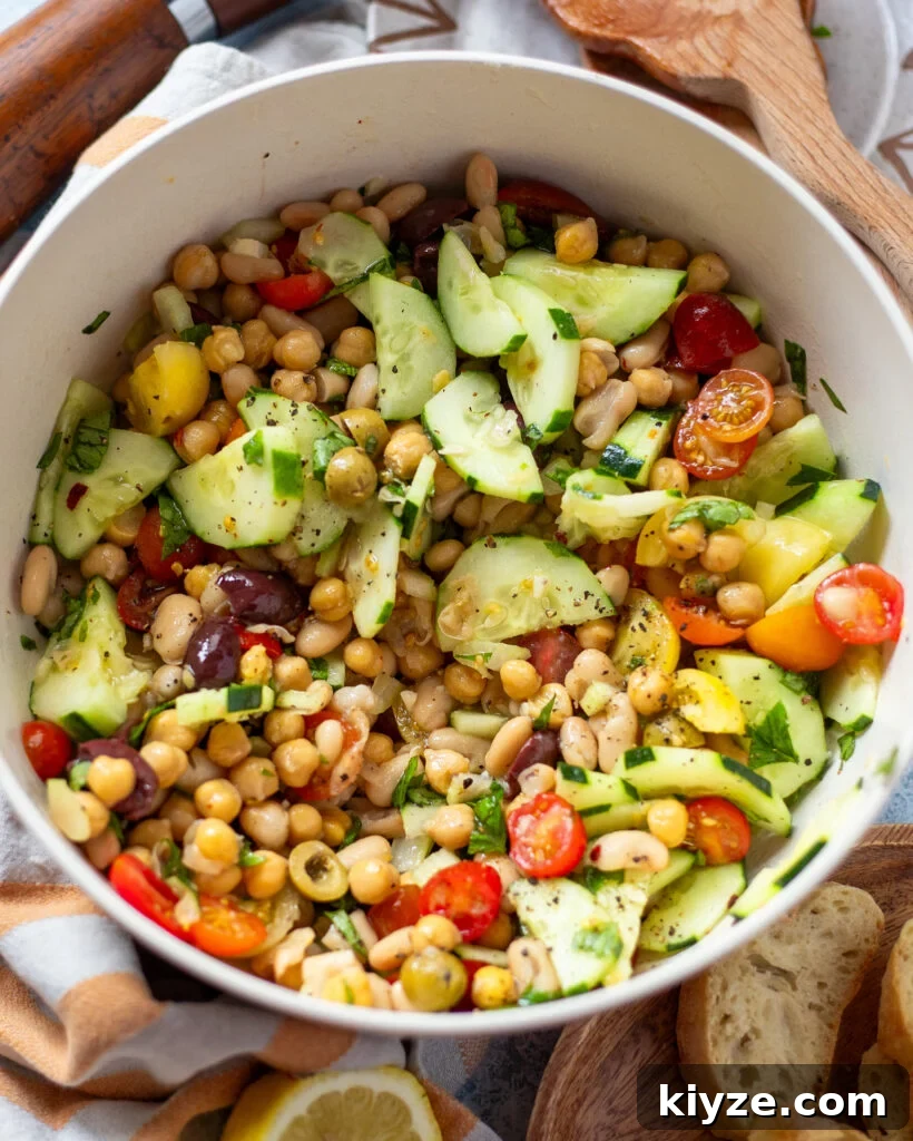 18 Flavorful Vegan Bean Salad Recipes for Every Occasion 3 overhead view of a white serving bowl holding a dense bean salad made with two types of canned beans, cucumber, tomato, celery and olives in a simple lemon and olive oil dressing.