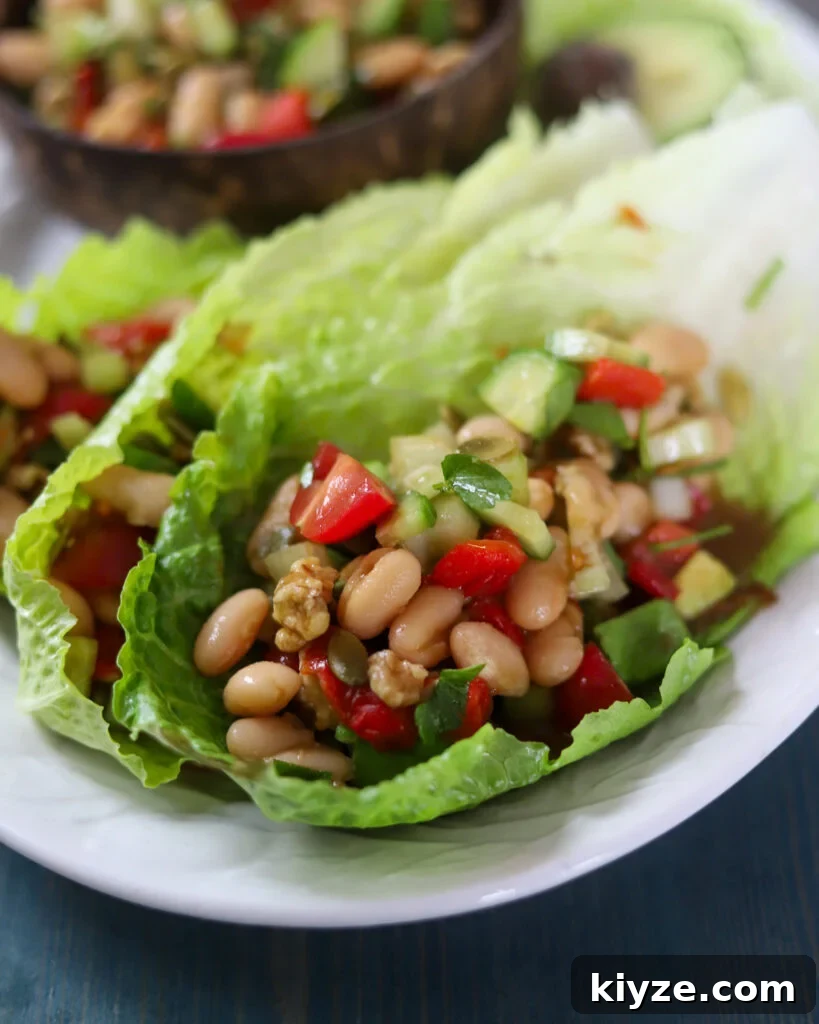 18 Flavorful Vegan Bean Salad Recipes for Every Occasion 6 White bean salad with tomatoes, celery, cucumbers, walnuts and avocado with miso dressing on a lettuce leaf on a white platter with other bowls of salad in the background