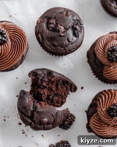 Blackberry Chocolate Cupcakes Recipe with Rich Ganache Filling 11 completed Blackberry Chocolate Cupcakes with one crumbled into two halves against a white surface