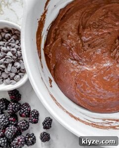 Blackberry Chocolate Cupcakes Recipe with Rich Ganache Filling 6 post mixing of wet and dry ingredients for Blackberry Chocolate Cupcakes in white bowl with chocolate chips and blackberries in the background