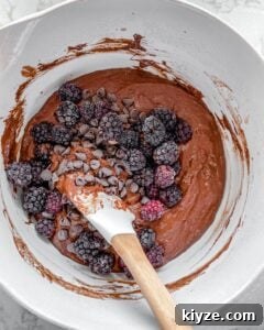 the addition of blackberries and chocolate chips added into Blackberry Chocolate Cupcakes batter in white bowl