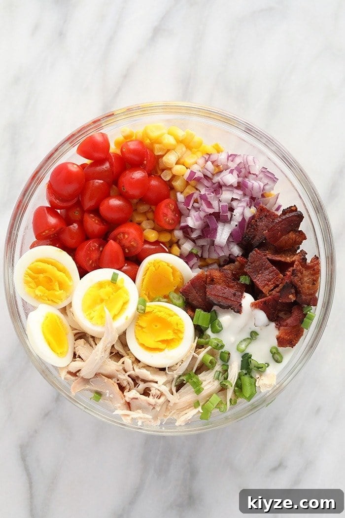 Your lunch for the week is ready in less than 30 minutes with this protein-packed Rotisserie Chicken Cobb Salad! rotisserie chicken cobb salad ingredients in a bowl ready to be mixed