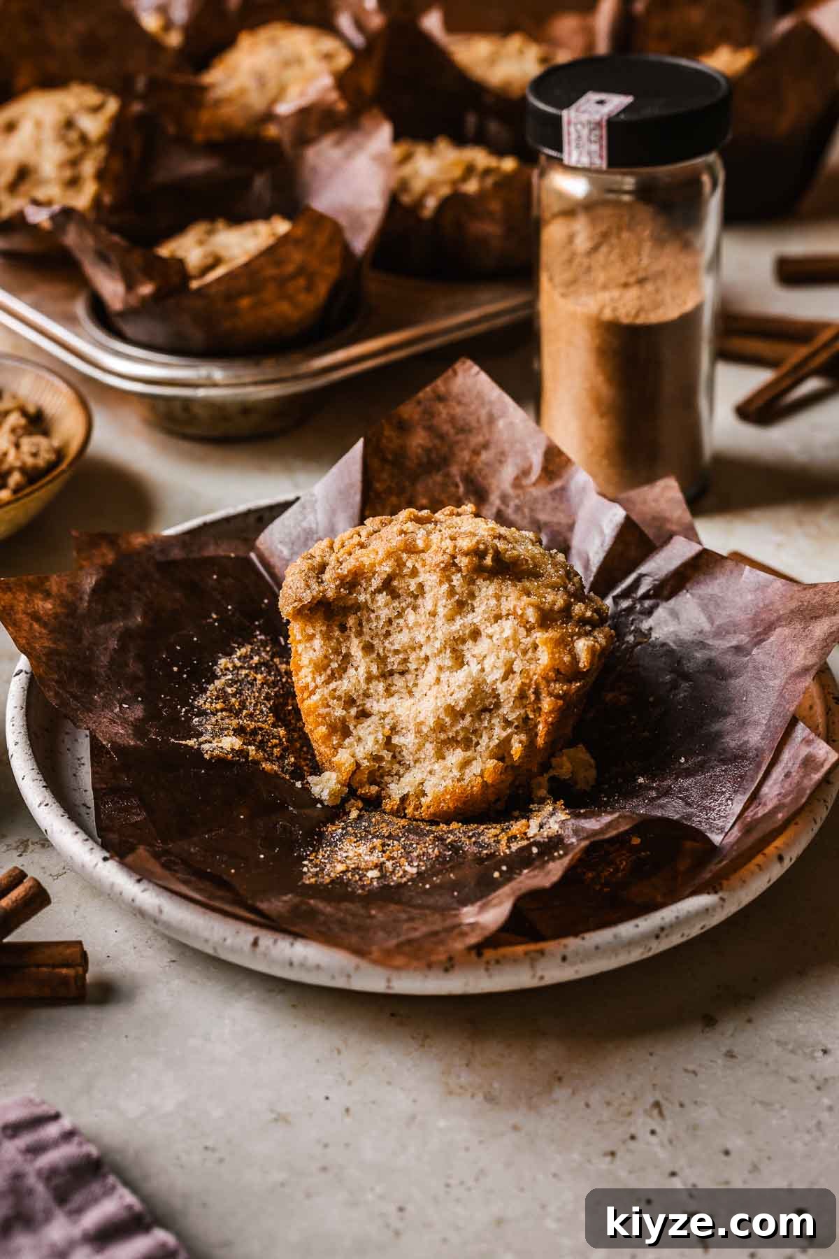 Cinnamon Streusel Muffins Recipe with Crunchy Brown Sugar Topping 12 An unwrapped cinnamon streusel muffin on brown parchment on a plate.