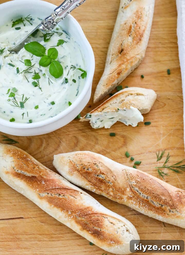 A wooden cutting board with small baguettes sliced open with a white bowl of whipped creamed cheese spread on a slice.