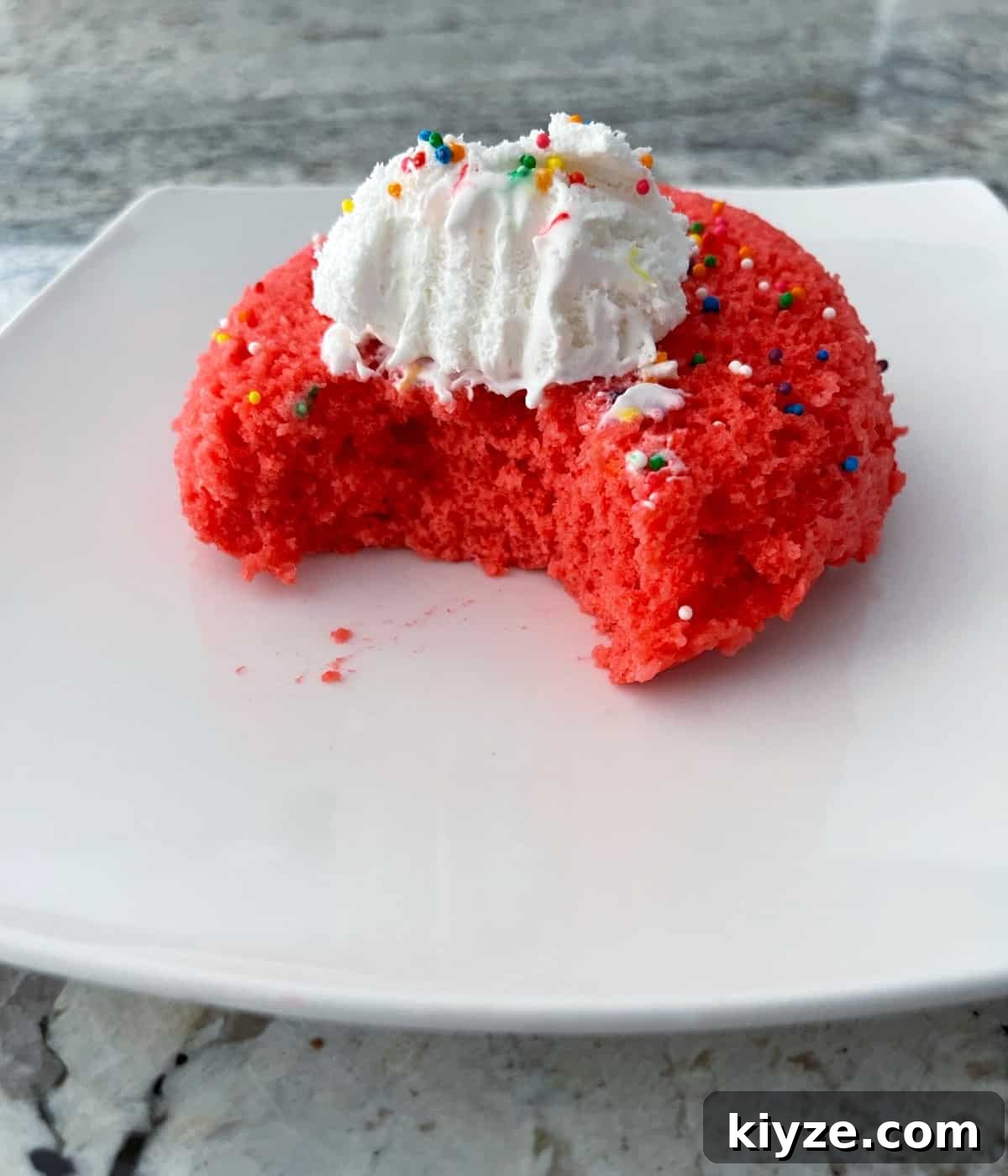 Microwave Mug Jello Cake Recipe: Quick Single-Serve Dessert 9 Single serving Raspberry Jello Mug Cake with sprinkled and whipped topping on white plate.
