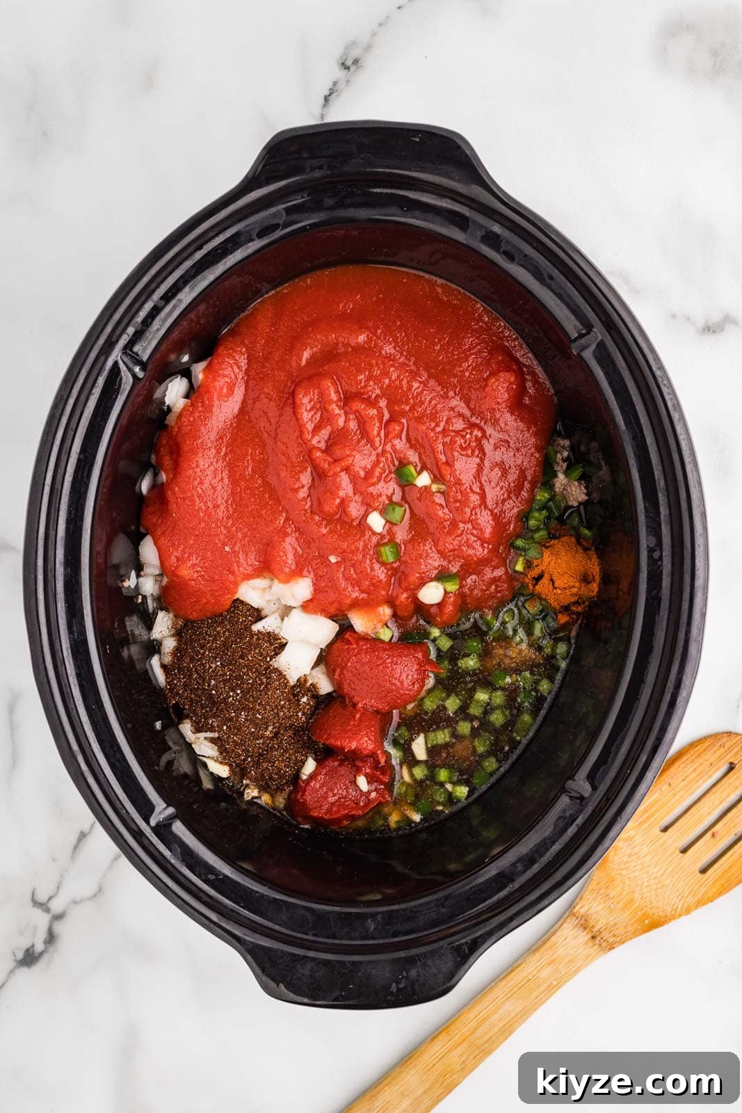 Slow Cooker No-Bean Chili Recipe for Tender, Flavorful Meat 6 overhead view of black slow cooker with all ingredients with wooden spoon on side