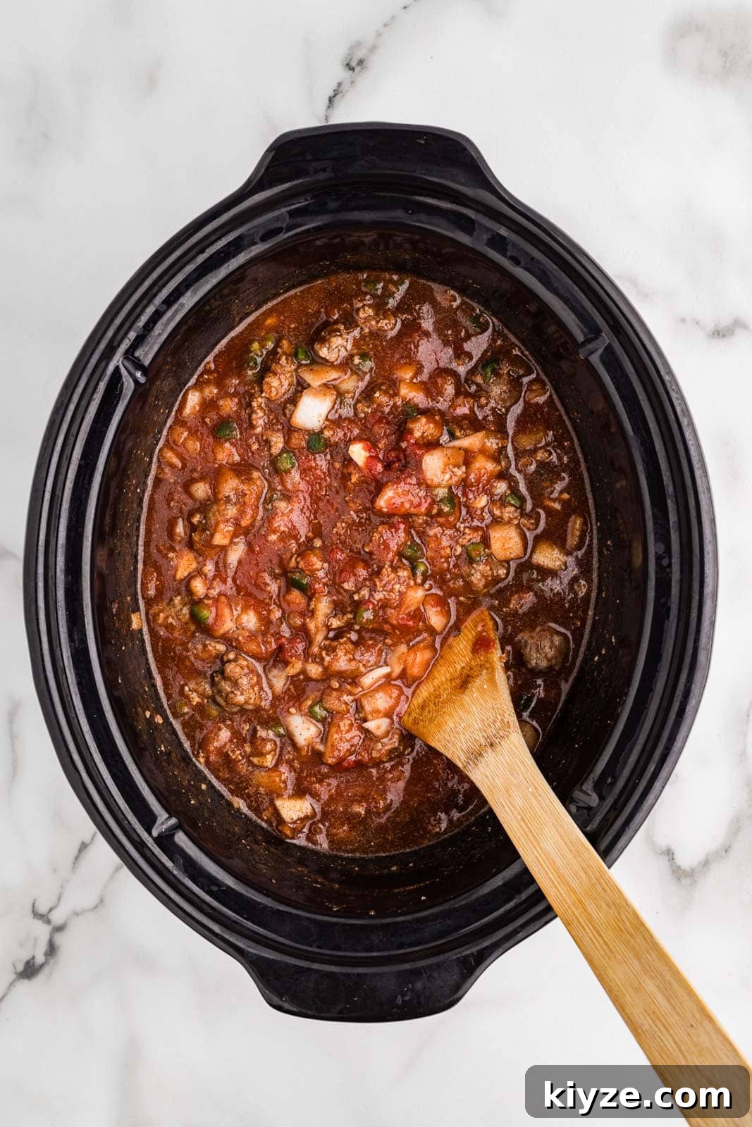 Slow Cooker No-Bean Chili Recipe for Tender, Flavorful Meat 7 overhead view of black slow cooker with all ingredients stirred with wooden spoon