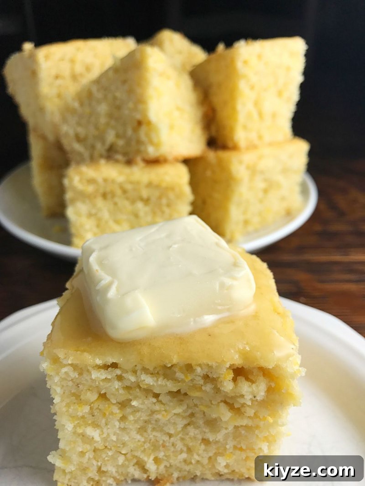 Sweet Dairy-Free Cornbread cut into pieces at stacked on a plate in the background with a single piece on a small white plate in front of it.