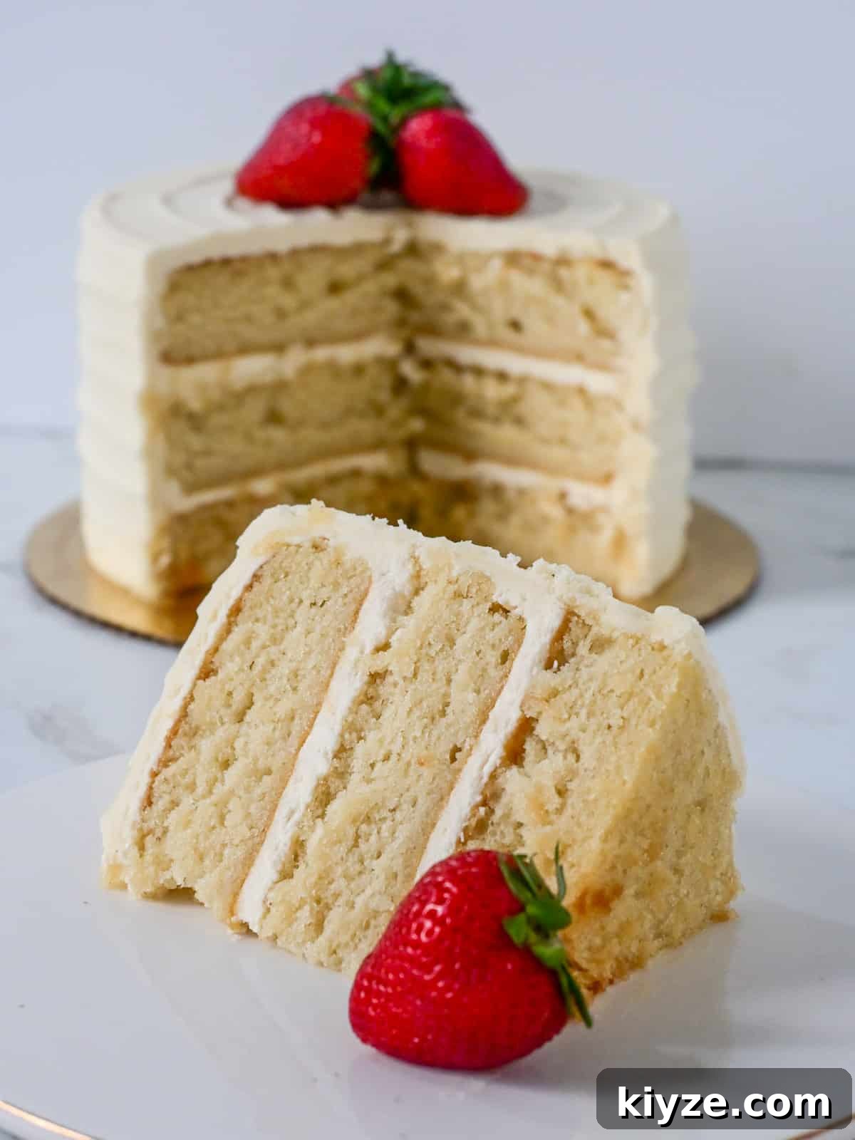 Moist Vanilla Cake Recipe Using the Reverse Creaming Method 12 close up view of a slice of vanilla cake made using the reverse creaming method with vanilla buttercream and strawberries for decoration.