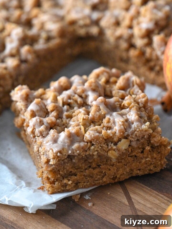 slice of moist applesauce crumb cake on parchment paper next to the rest of the cake and fresh apples.