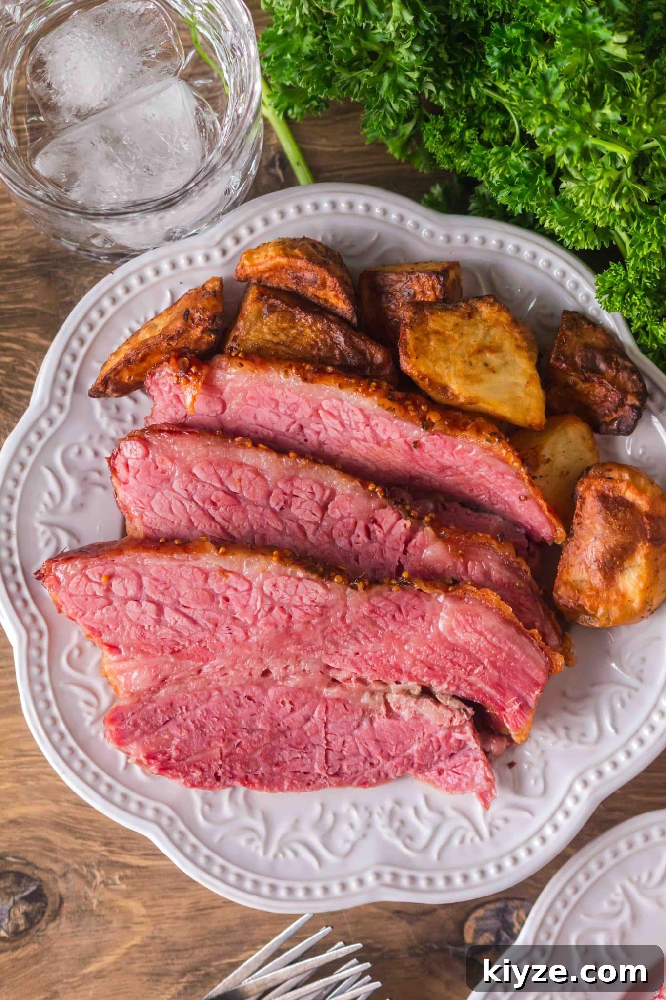 Juicy Oven-Baked Corned Beef Brisket Recipe 8 Top down view of a white plate filled with sliced oven-baked corned beef and roasted potatoes. Hostess At Heart