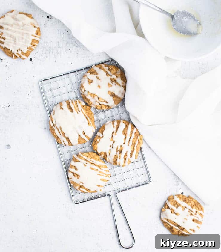 brown butter iced pumpkin cookies on a small silver cooling rack next to a piece of white linen and a bowl.