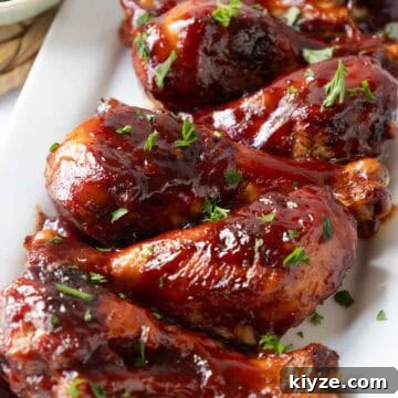 Crispy Oven-Baked BBQ Chicken Drumsticks 12 A close view of several barbecue glazed chicken drumsticks shows the thick, shiny coating and small herb garnish on top. The texture of the sauce and crisped skin is clearly visible.