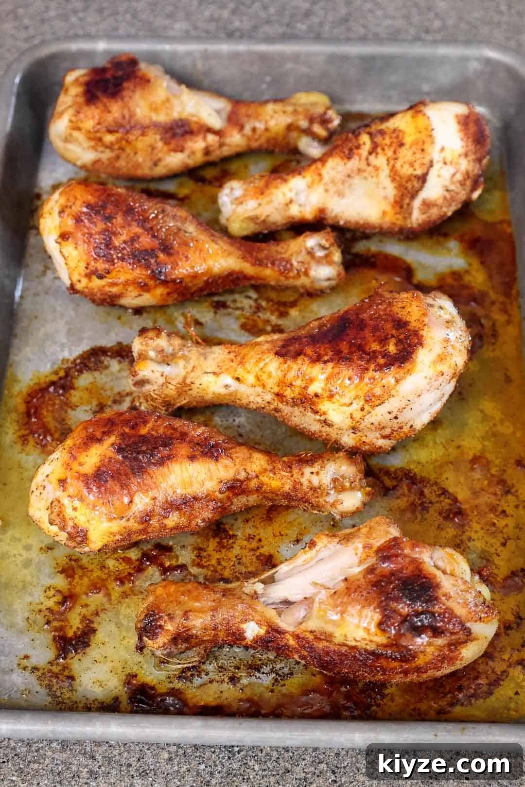 Crispy Oven-Baked BBQ Chicken Drumsticks 5 Partially cooked chicken drumsticks bake in a tray with rendered juices and browned seasoning on the surface. The skin is beginning to crisp and develop color.
