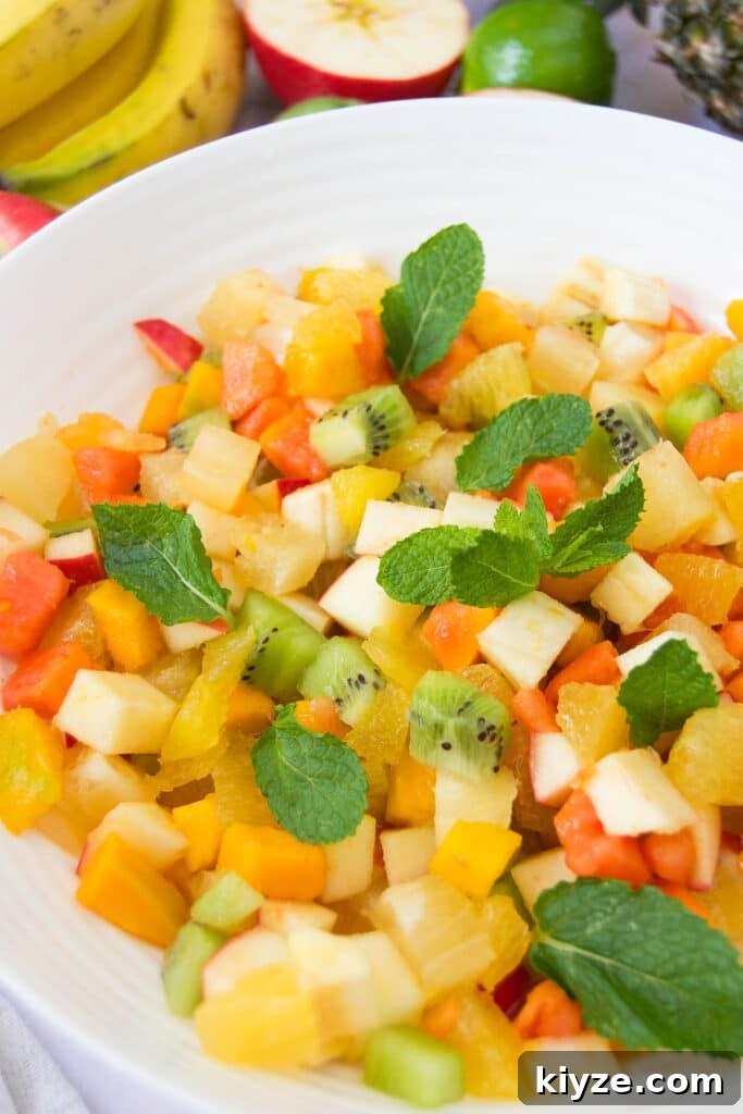 Tropical Fruit Salad with Mango, Pineapple and Coconut 2 close up of a white bowl holding a serving of tropical fruit salad garnished with mint leaves