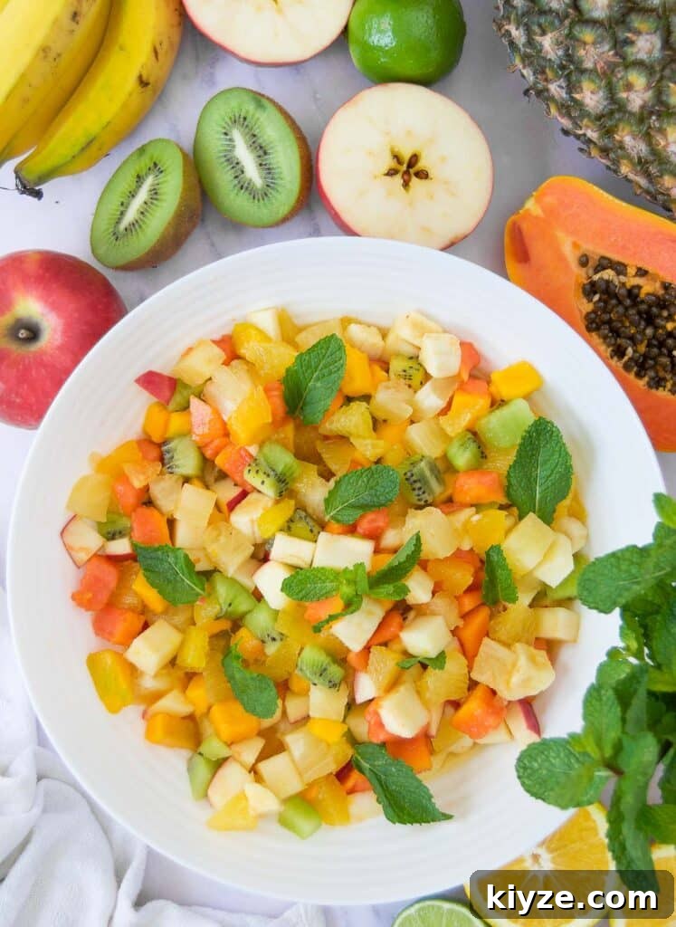 Tropical Fruit Salad with Mango, Pineapple and Coconut 3 a white bowl holding diced tropical fruit salad surrounded by halved tropical fruits on marble