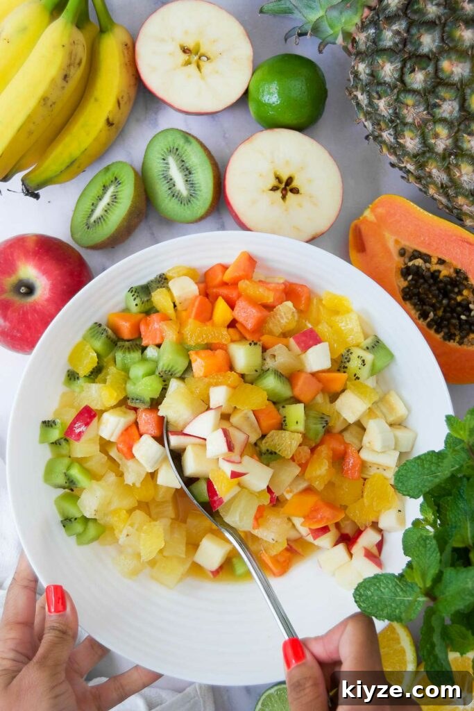 Tropical Fruit Salad with Mango, Pineapple and Coconut 6 a spoon stirs an easy fruit salad surrounded by halved tropical fruits