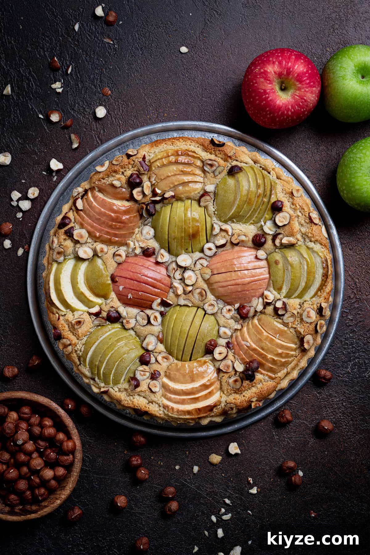 Vegan Apple Hazelnut Frangipane Tart 2 Vegan apple hazelnut frangipane tart on a dark background with apples and a bowl of hazelnuts.