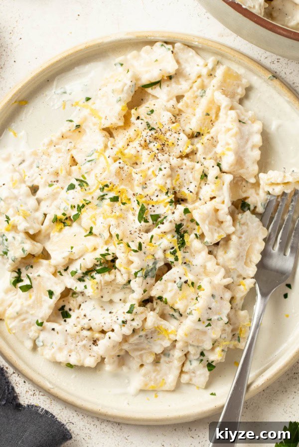A fork digging into cream cheese pasta on a white plate.