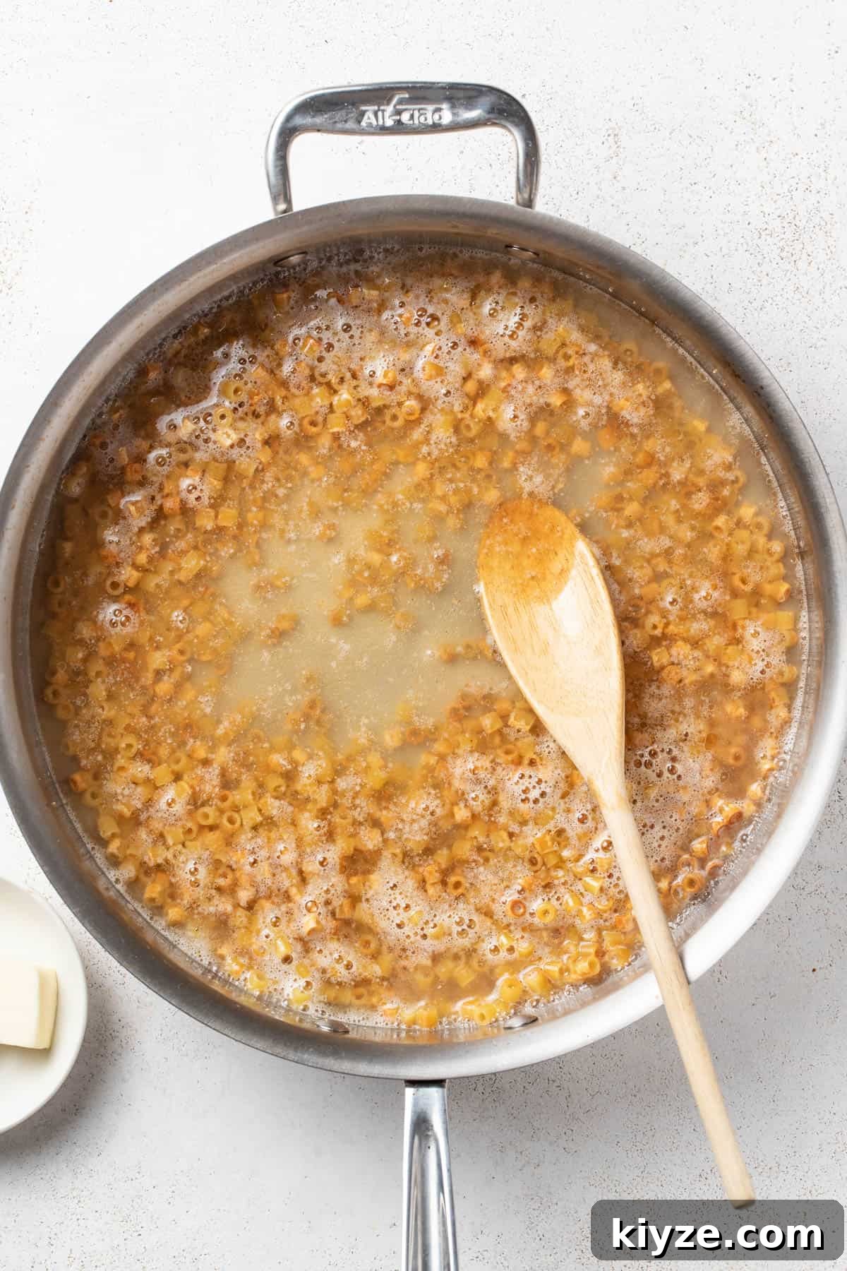 Adding broth to the skillet with the butter and pasta.