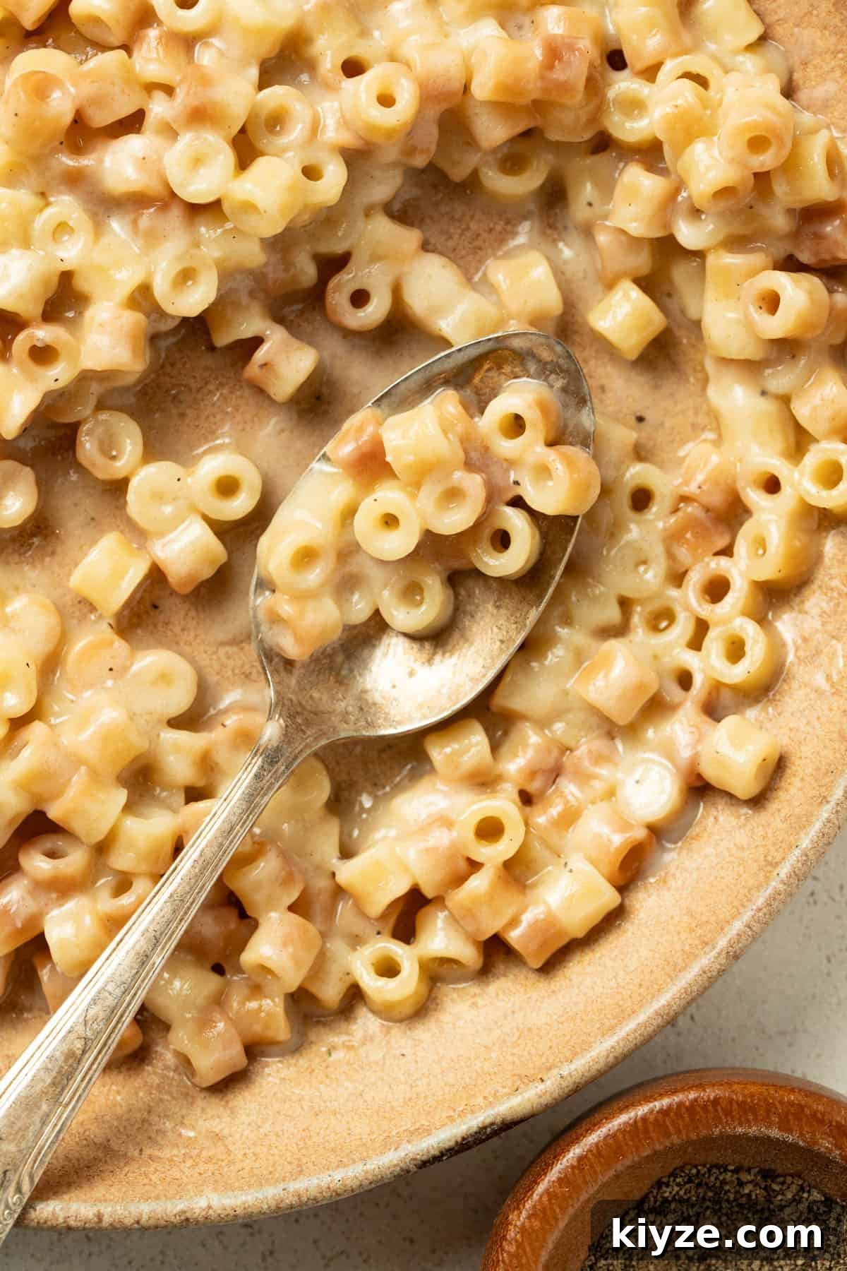 A spoon dipping into a bowl with buttered pasta noodles.