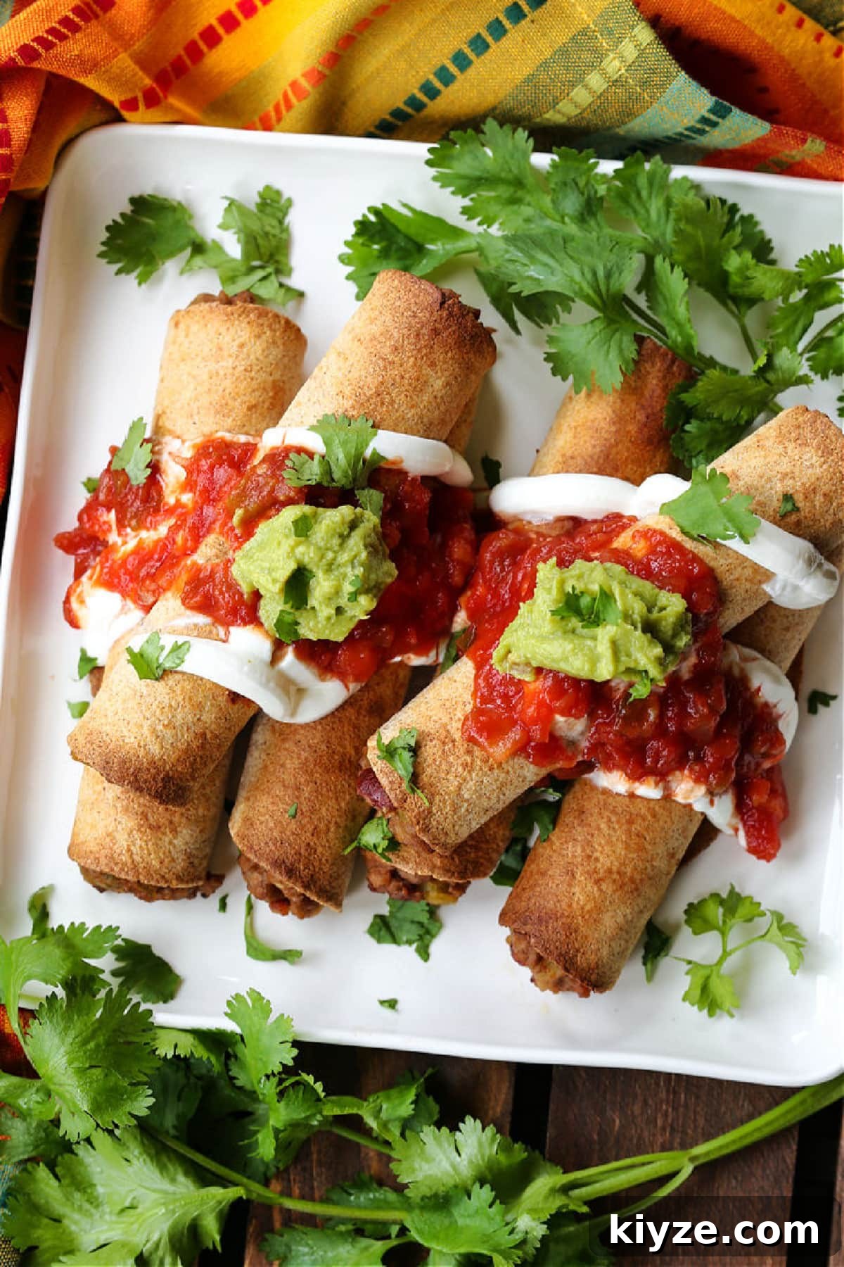 Crispy tortilla shells stuffed with a cheesy beef filling beef taquitos on a plate with salsa and guacamole
