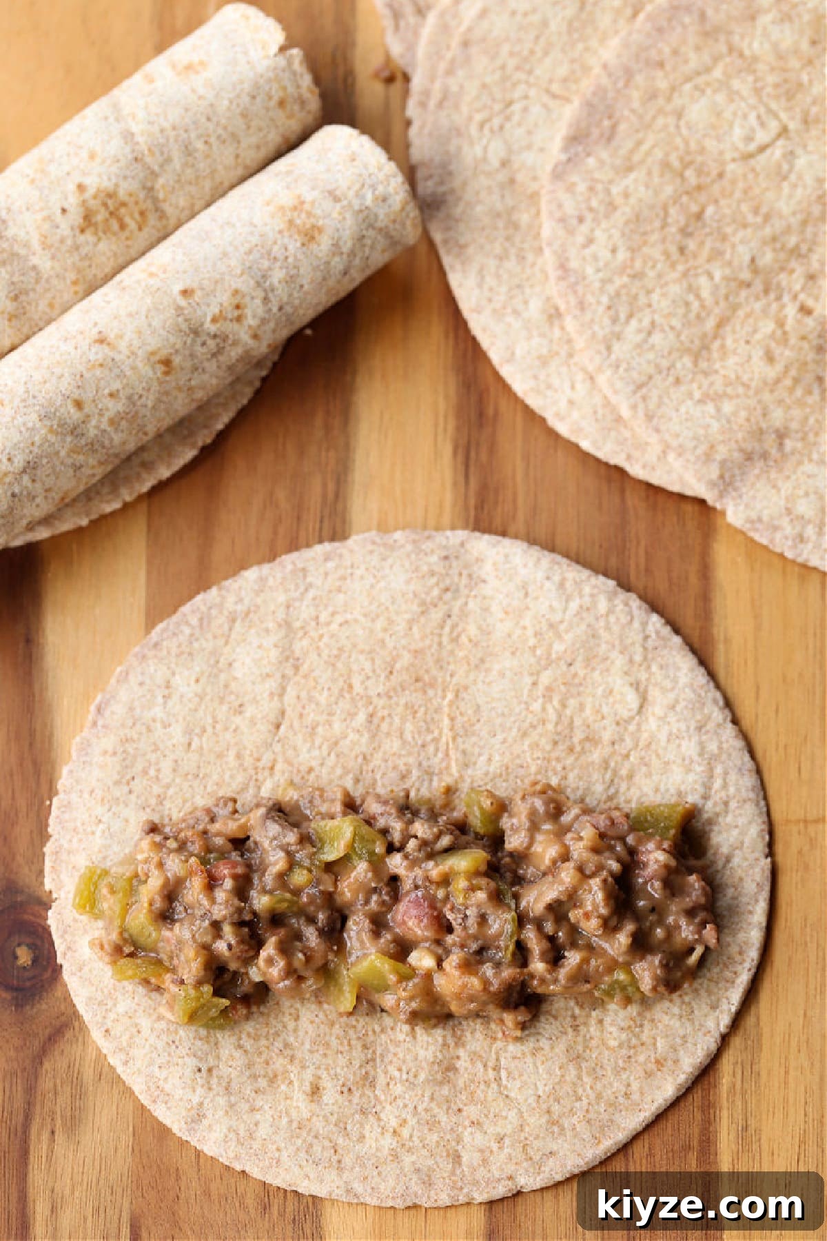 Assembling taquitos ground beef and cheese filling in a line across a tortilla