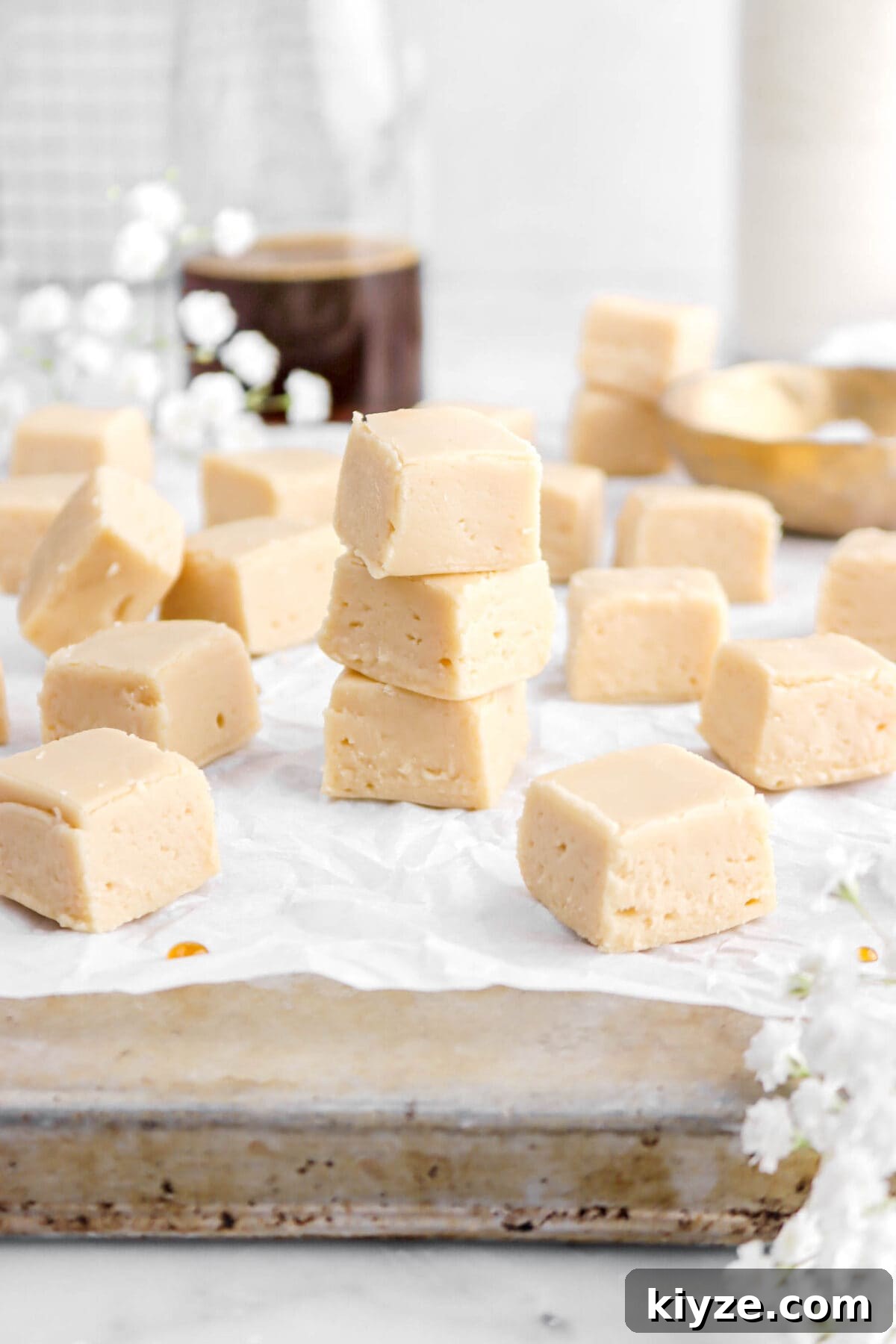 Old-Fashioned Maple Fudge Recipe 16 maple fudge stacked on parchment paper lined antique sheet pan with more pieces of fudge around.