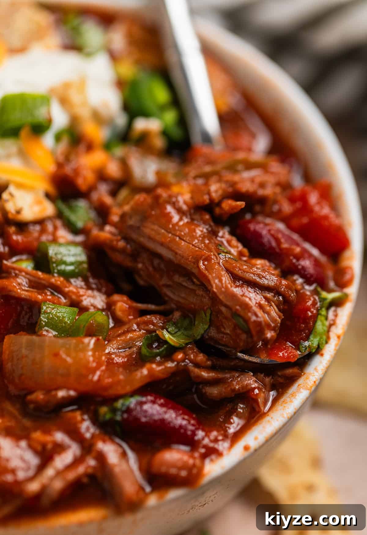 Slow Cooker Shredded Beef Chili Recipe 2 Bowl of shredded beef chili with spoon scooping into it.