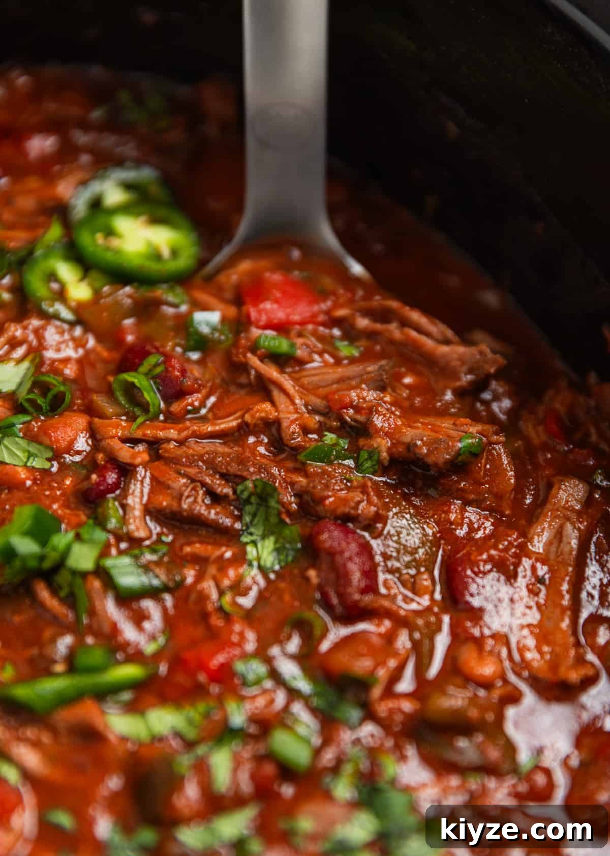 Slow Cooker Shredded Beef Chili Recipe 9 Slow cooker shredded beef chili in crockpot topped with cilantro and jalapeño with ladle.
