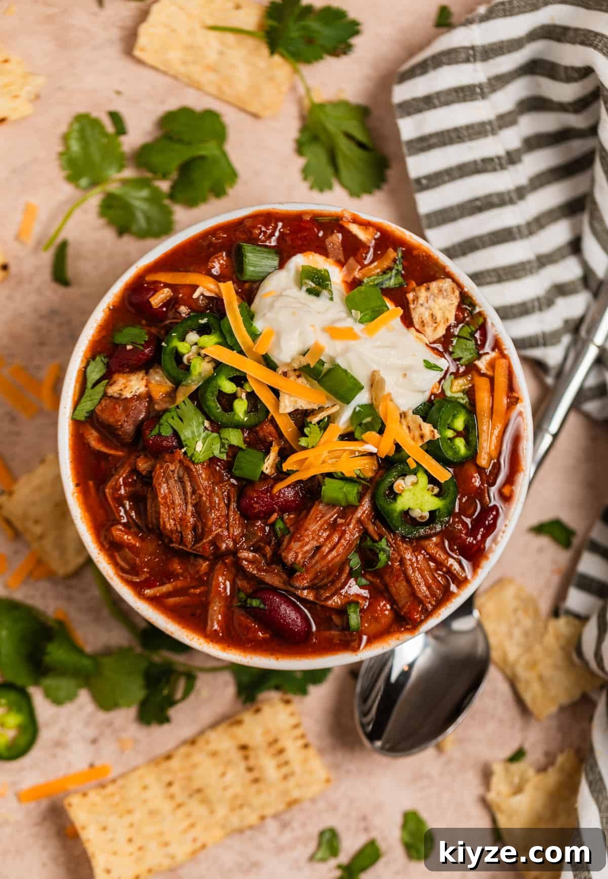 Slow Cooker Shredded Beef Chili Recipe 10 Overhead view of chili in bowl topped with sour cream, cheese, cilantro and other toppings.