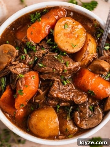 White bowl with crockpot beef stew with mushrooms, carrots and potatoes topped with chopped parsley.