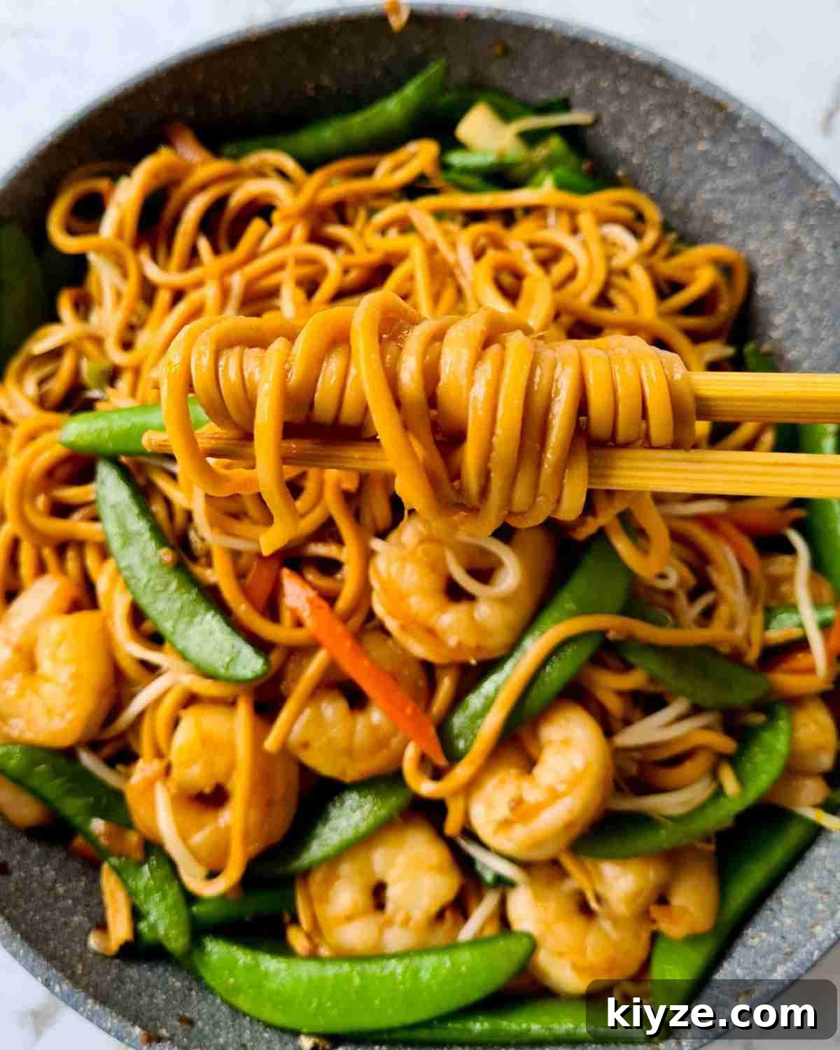 Wok Fried Prawn Noodles with Garlic and Chili 10 Thick noodles held up by a pair of chopsticks over a pan