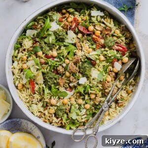 Pesto and orzo salad mixed in a large mixing bowl, with silver tongs.